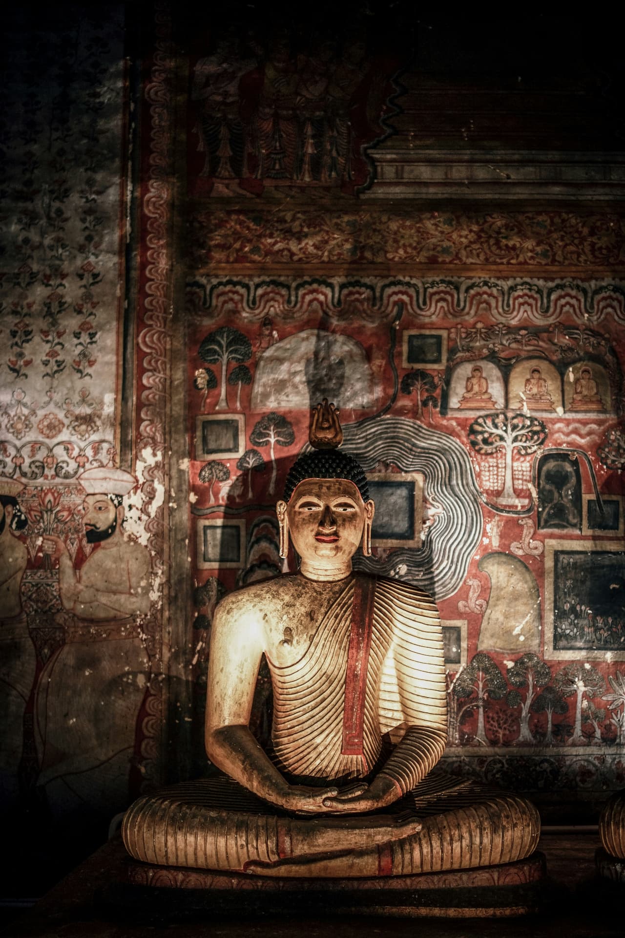 Golden Buddha statue against ancient painted murals in a Sri Lankan cave temple